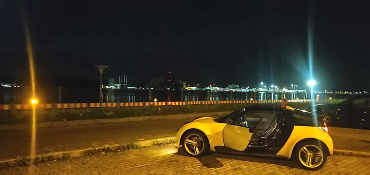 Gelber Smart Roadster mit offener Tür am nächtlichen Ufer